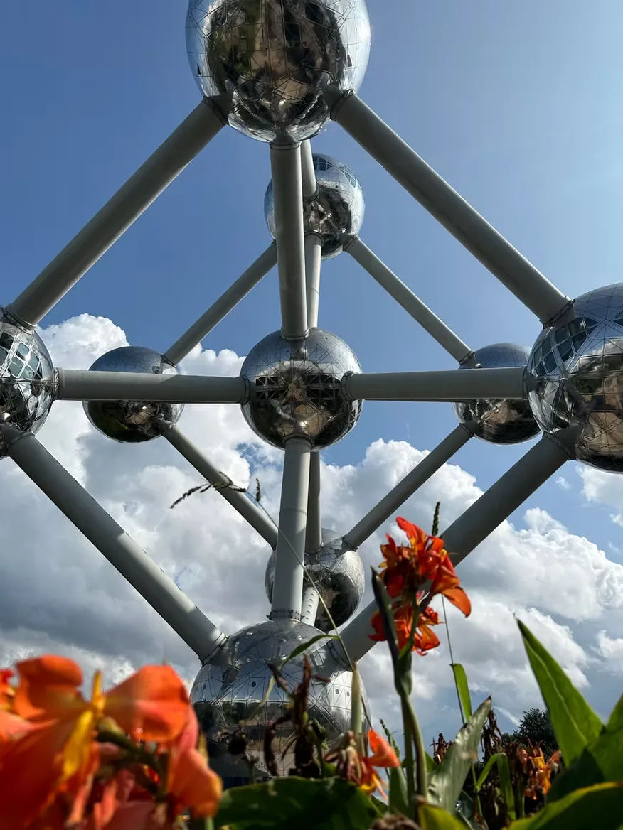 Mirrored steel spheres joined by tubes rising into cloud, orange flowers in the foreground.
