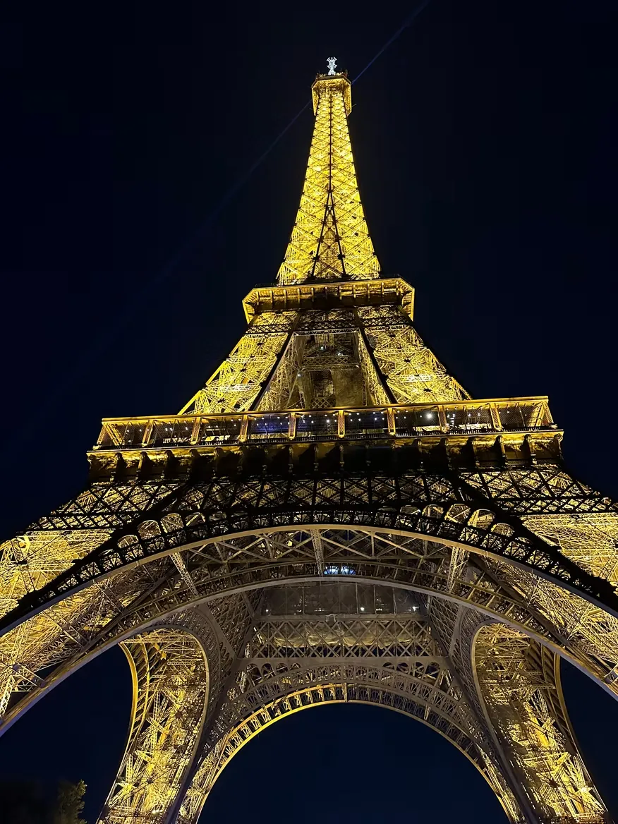 The Eiffel Tower lit gold at night, photographed from directly beneath the arch.